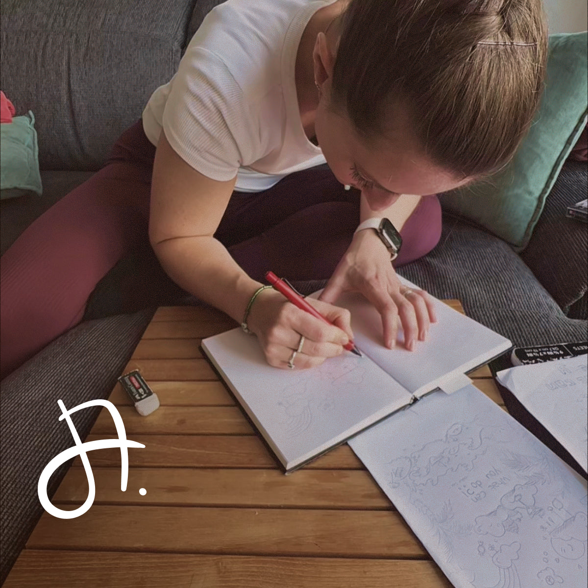 Frau skizziert mit rotem Stift in einem Notizbuch auf dem Sofa.